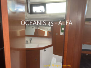 Bathroom aboard an Oceanis 45 yacht, featuring a white sink, wood cabinets, mirror, and an overhead hatch.