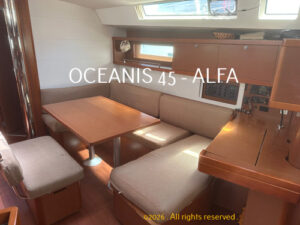 Sailboat cabin interior with beige seating around a wooden table and a navigation station on the right.